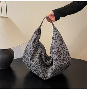 Detailed view of a large leopard print tote bag held by a person in a minimalist room