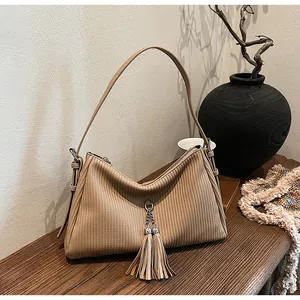 Detail of khaki corduroy tote bag with dual tassels on a dark wooden surface
