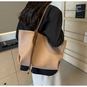 Detail of a large woven tote bag with brown leather straps shown on a model