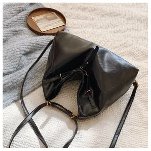 Detalle del bolso minimalista de cuero sintético negro con forma de triángulo plegado y ojales