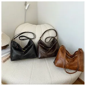 Detalle de tres bolsos hobo retro grandes en negro, marrón y camel sobre un sofá blanco