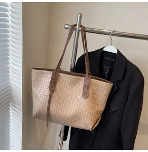 Detail of woven tote bag with brown leather straps and textured beige finish on a hanger