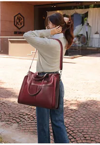 Détail du grand sac cabas bordeaux porté par un mannequin contre un mur en briques