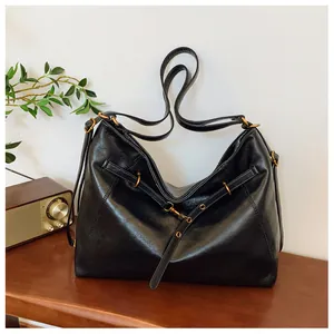 Detalle de bolso tote grande de cuero negro con herrajes dorados retro en mesa de madera