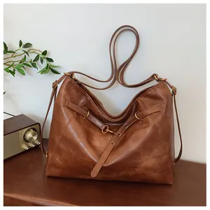 Detalle de bolso tote vintage de cuero marrón con gancho de metal sobre escritorio madera