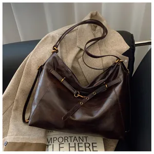 Detalle de un bolso tote grande de cuero marrón oscuro con hebilla dorada sobre abrigo