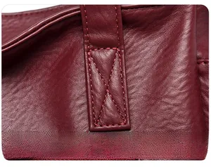 Gros plan des coutures renforcées sur la bandoulière d'un sac cabas en cuir bordeaux