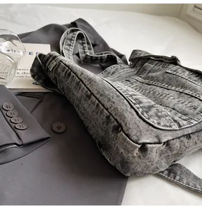 Detailed view of grey washed denim messenger bag texture and flap on grey blazer background