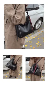 Detail showing the black textured PU leather bag with decorative red patterned strap accessory