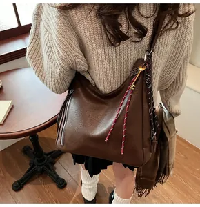 Close-up of brown PU leather hobo bag with metal zipper and red woven tassel detail