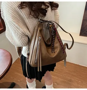 Close-up of brown textured leather backpack featuring long tassels and woven cord charm