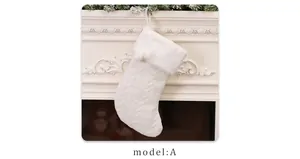 Close-up of a white cable knit Christmas stocking with plush trim hanging on a fireplace