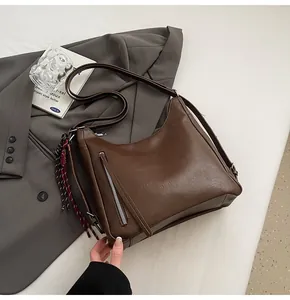 Detail view of brown PU leather hobo bag with metal zipper and woven tassel charm