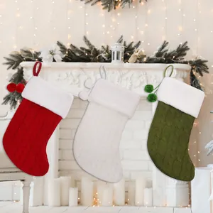 Set of 3 cable knit Christmas stockings with plush faux fur trim and pom-poms on a fireplace