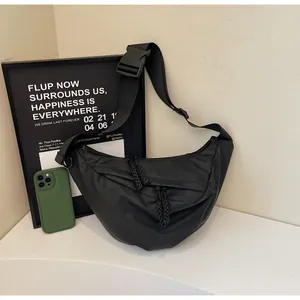 Detail of black nylon crescent bag featuring wide strap, plastic buckle, and rope pullers