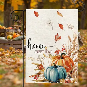Close-up of autumn garden flag featuring printed pumpkins, fallen leaves and wheat stalks.