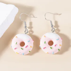 Detail of pink resin donut earrings with white cream frosting and colorful sprinkles