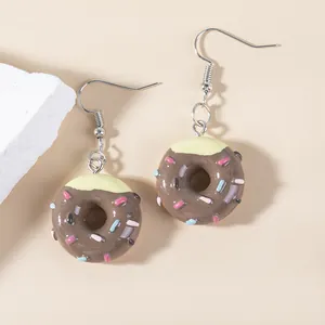 Close-up of chocolate-colored donut earrings with cream frosting and sprinkles on beige backdrop