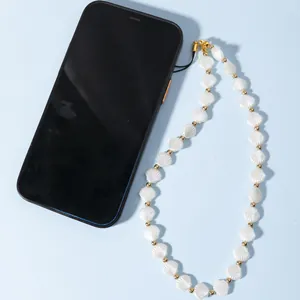 Dragonne de téléphone en coquillages blancs avec perles dorées sur fond bleu pastel