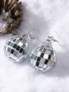 Macro detail of disco ball earrings with reflective mirrors on snowy pine background