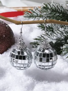 Close-up of silver disco ball drop earrings on festive pine branch with snow background