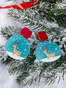 Detailed view of Christmas acrylic earrings with reindeer motifs on snowy pine branches