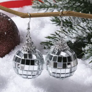 Silver disco ball drop earrings hanging on a winter tree branch with festive decorations