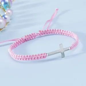 Dettaglio del bracciale a cordoncino rosa intrecciato a mano con croce d'argento lucido