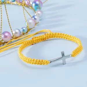 Dettaglio del bracciale in corda gialla intrecciata con croce d'argento su sfondo blu