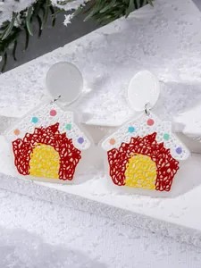 Macro shot of gingerbread house acrylic earrings on snow with pine branches