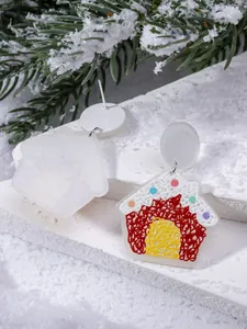 Detailed view of colorful acrylic gingerbread house earrings on festive snowy branches