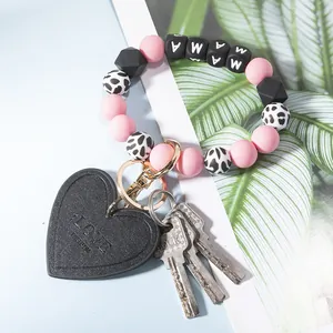Detail of beaded MAMA keychain with pink beads and leather heart charm on blue backdrop