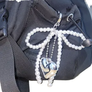 Elegant pearl bow keychain with a silver heart pendant on a black textured backpack