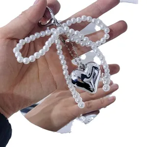 Fashionable faux pearl bow keychain with silver heart pendant held in hand for bag decor