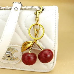 Red glitter cherry keychain with gold leaves as a charm for a white leather handbag