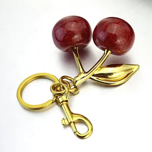 Macro detail of red glitter cherry keychain with gold metal leaves and snap hook