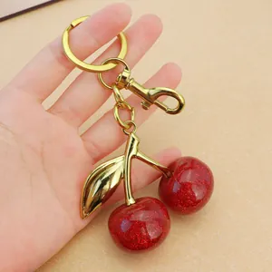 Macro detail of red cherry keychain featuring glitter resin finish and gold metallic hardware