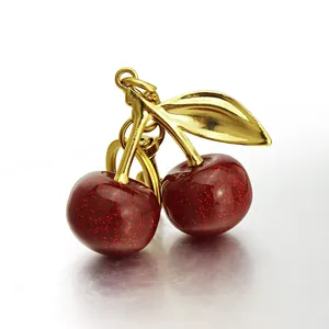 Detailed view of red cherry resin charms with glitter and golden metal leaf on a keychain