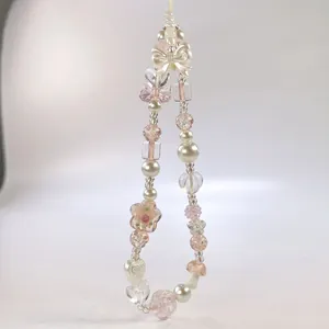 Détail d'une dragonne de téléphone en cristal rose et blanc avec breloques nœud et cœur