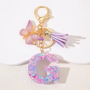 Detail of glitter resin letter G keychain with purple butterfly and tassel accessory