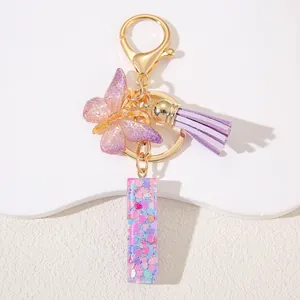 Macro detail of resin letter keychain with pink sequins, purple tassel, and gold lobster clasp