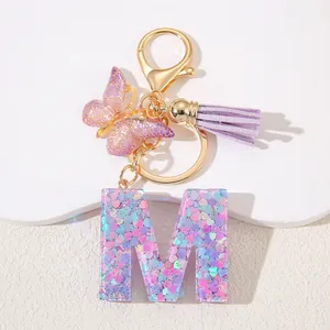 Detail of pink sequin resin letter M keychain with purple butterfly and tassel charm