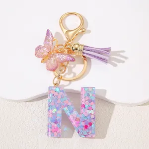 Detail of resin letter N keychain with pink sequins, purple butterfly, and silk tassel charm