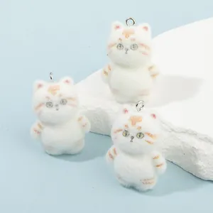 Three flocked cat charms with orange stripes on a stone base with light blue background