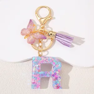 Close-up of pink resin letter R keychain with sequins, butterfly charm and purple tassel