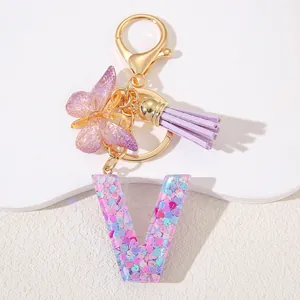 Detail of resin letter V keychain with purple sequins, gold clasp, butterfly and tassel