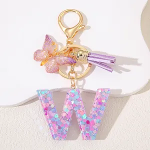 Detail of glitter resin letter W keychain with purple butterfly and leather tassel charms
