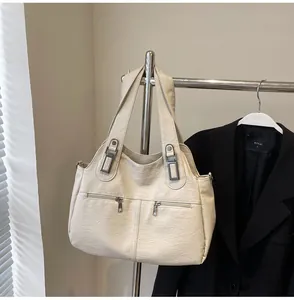 Detail van de crème kunstleren tote tas met zilveren ritsvakken en metalen gespen