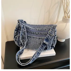 Detail view of washed denim crossbody bag featuring three zipper pockets and silver buckle