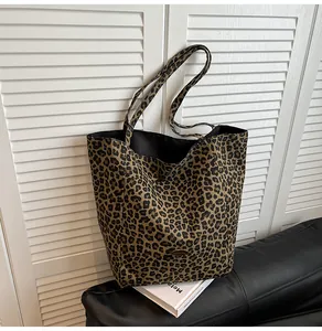 Detail shot of leopard print canvas tote bag leaning against a black leather sofa with white props